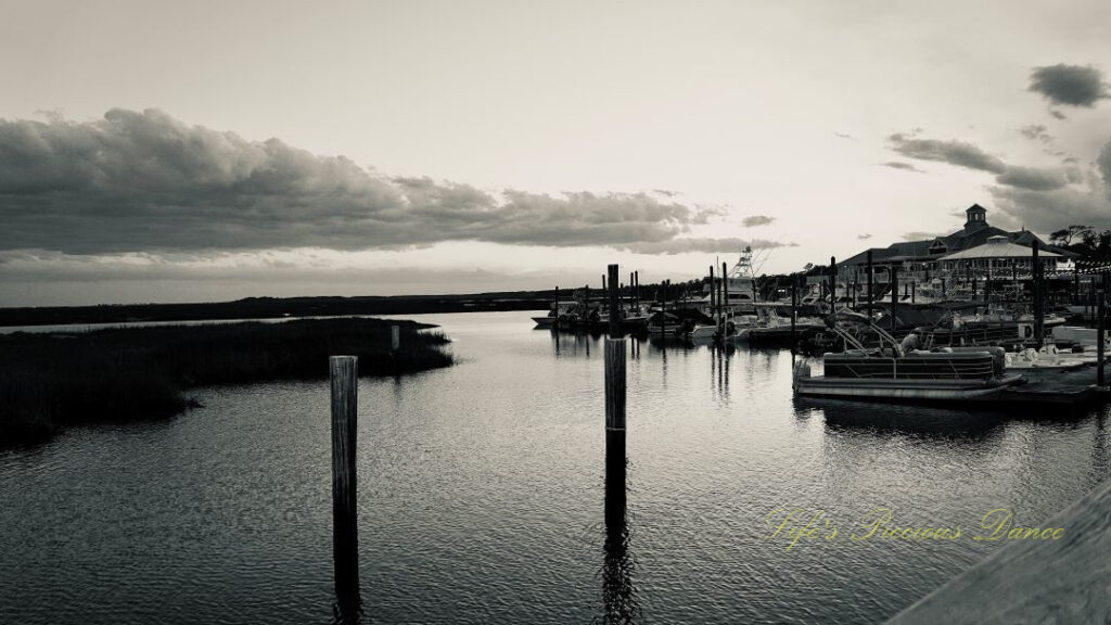 Black and white of boats along a dock at Murrells Inlet. Passing clouds overhead.