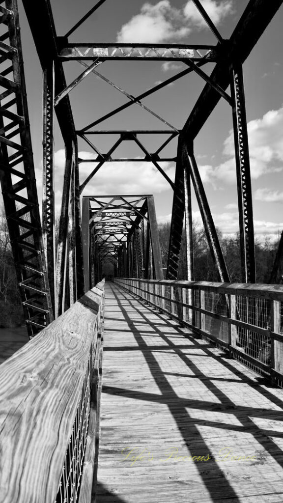 Black and white straight on view of an old train trestle turned walking bridge.