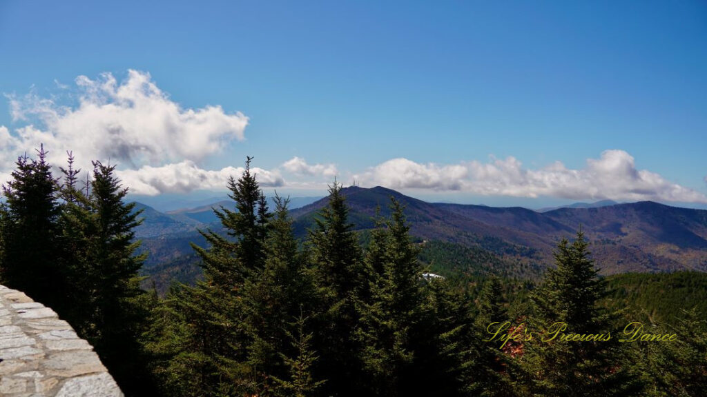 Landscape view from the top of Mt Mitchell overlooking colorful mountain peaks and trees in the valley. Passing clouds above.