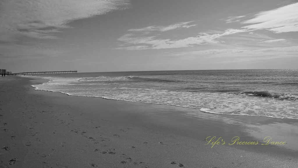 Black and white of waves rolling into and over the beach. Passing clouds up above.