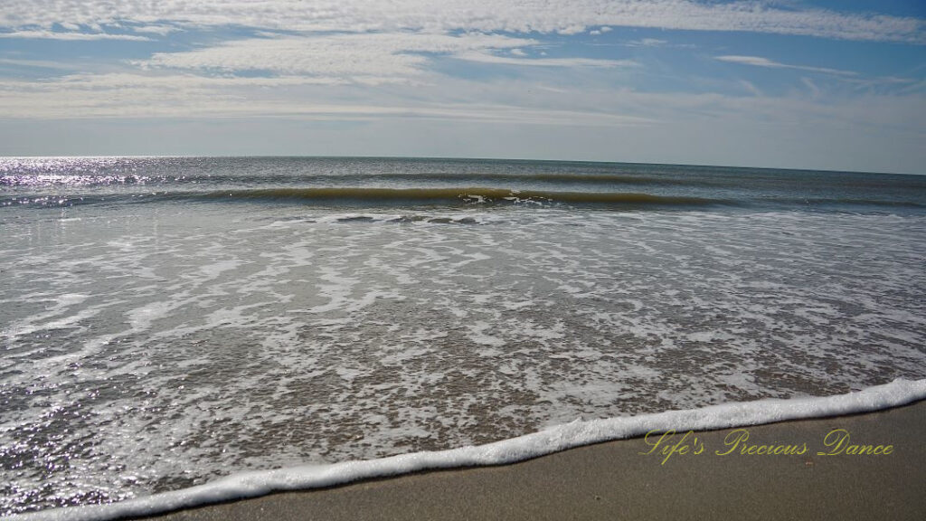 Frothy ocean waves rolling over the beach. Passing clouds overhead.