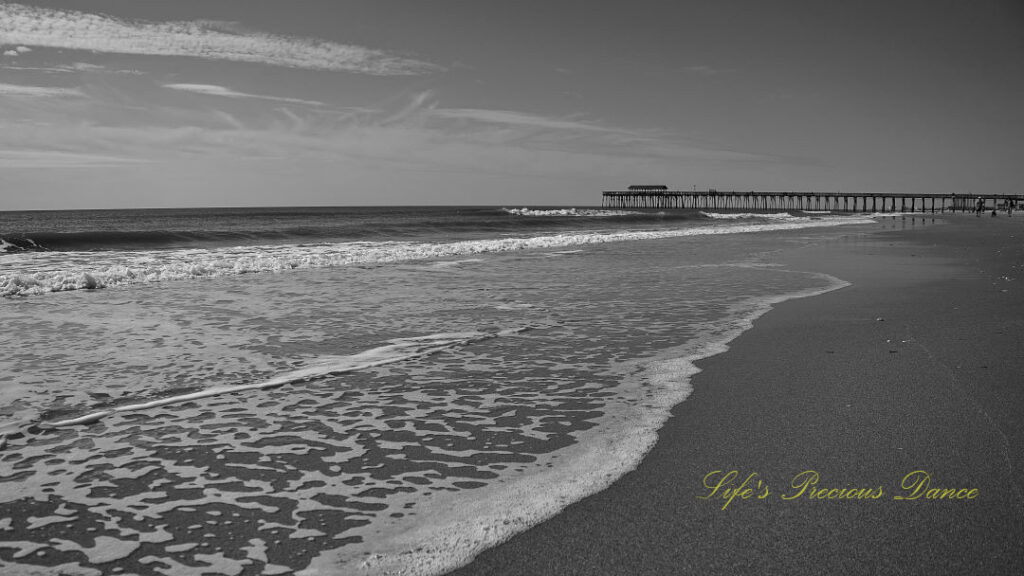 Black and white of waves crashing into the beach. Myrtle Beach pier in the background.