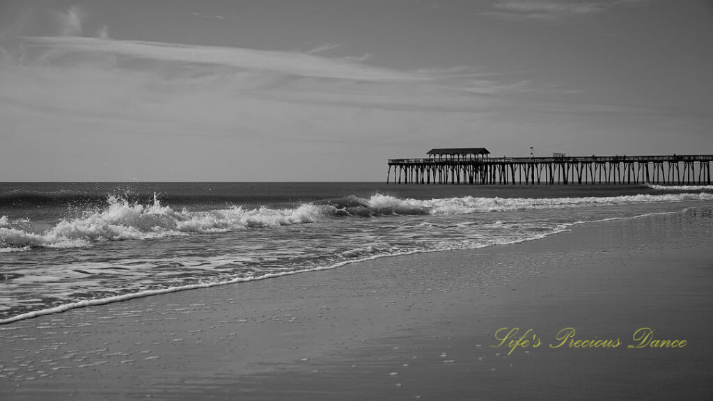 Black and white of waves crashing into the beach. Myrtle Beach pier in the background.