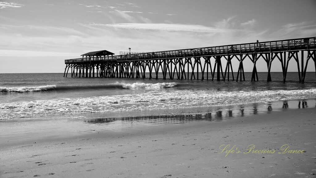 Black and white side view of the Myrtle Beach pier. Clouds overhead and waves rolling in.