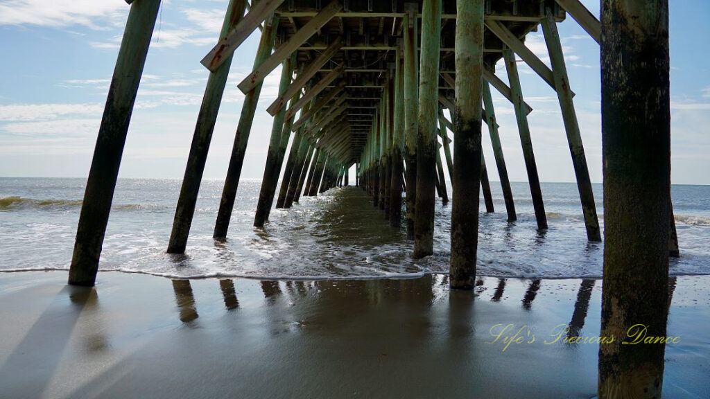 View from under the pier as ocean waves crash against the beach.