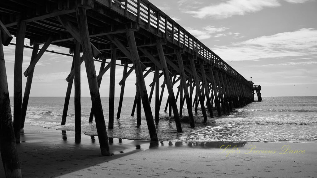 Black and white side view of the Myrtle Beach pier. Clouds overhead.