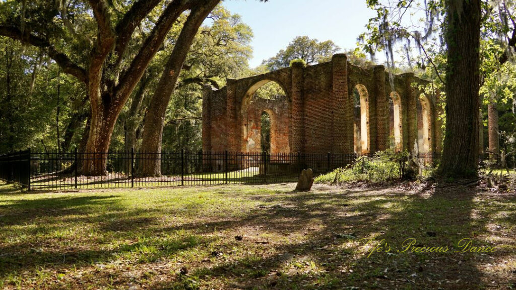 Rear side view of the Old Sheldon Church ruins. An old slanted tombstone stands to the side.