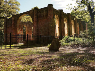 Rear side view of the Old Sheldon Church ruins. An old slanted tombstone stands to the side.