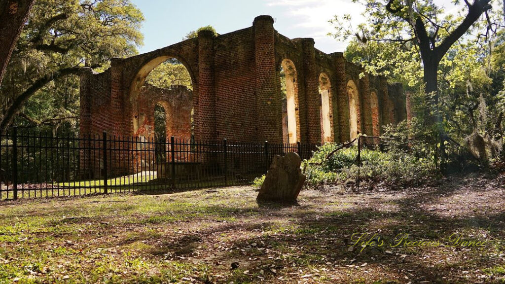 Rear side view of the Old Sheldon Church ruins. An old slanted tombstone stands to the side.