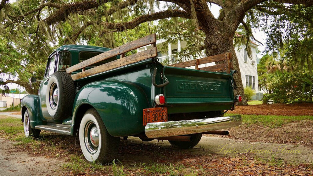 Close up rear and driver side view of a classic 1953 dark green Chevrolet 3100 truck.