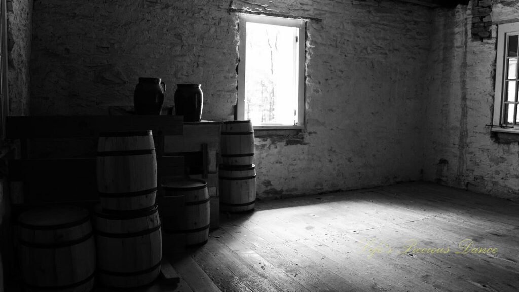 Black and white of stacked barrels and jugs on a wooden table inside a stone blockhouse at Oconee Station.