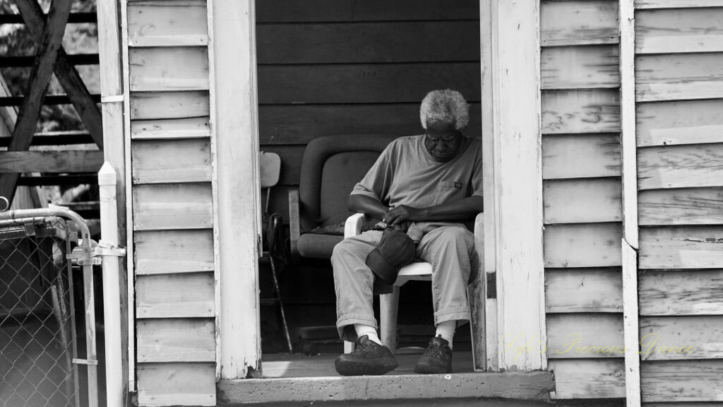 Black and white of man sleeping on a porch.