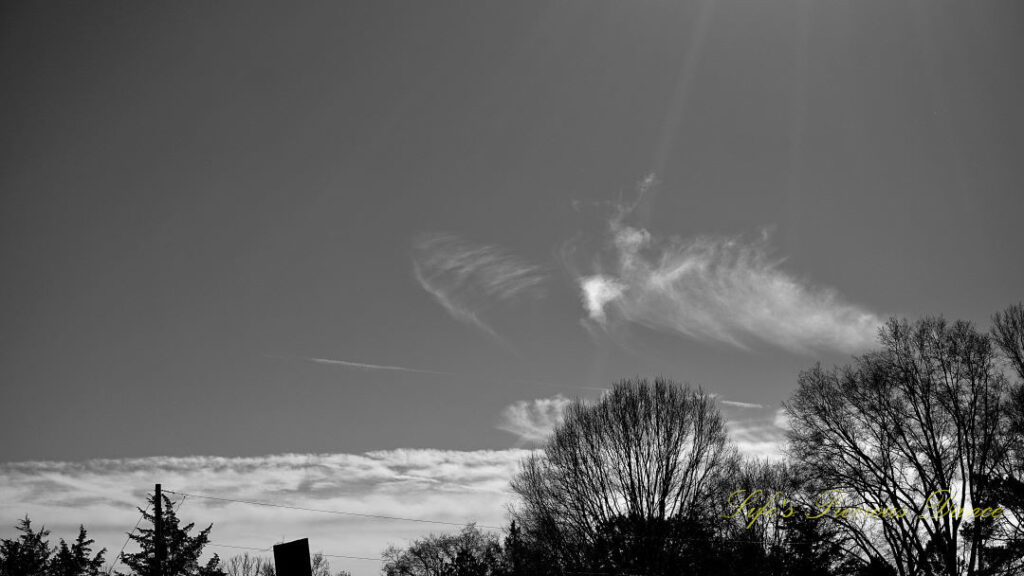 Black and white passing clouds in the shape of an angel. The sun&#039;s rays cascading down.