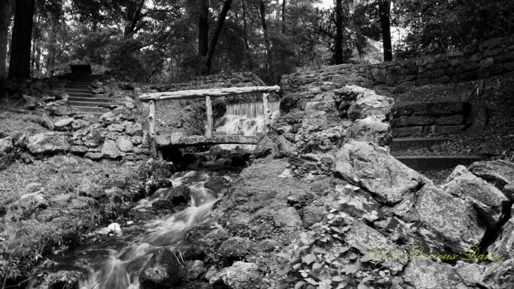 Black and white of the mini-waterfall spilling through the rocks at Poinsett State Park, surrounded by the old mill remnants. A small stone bridge crosses over the water.