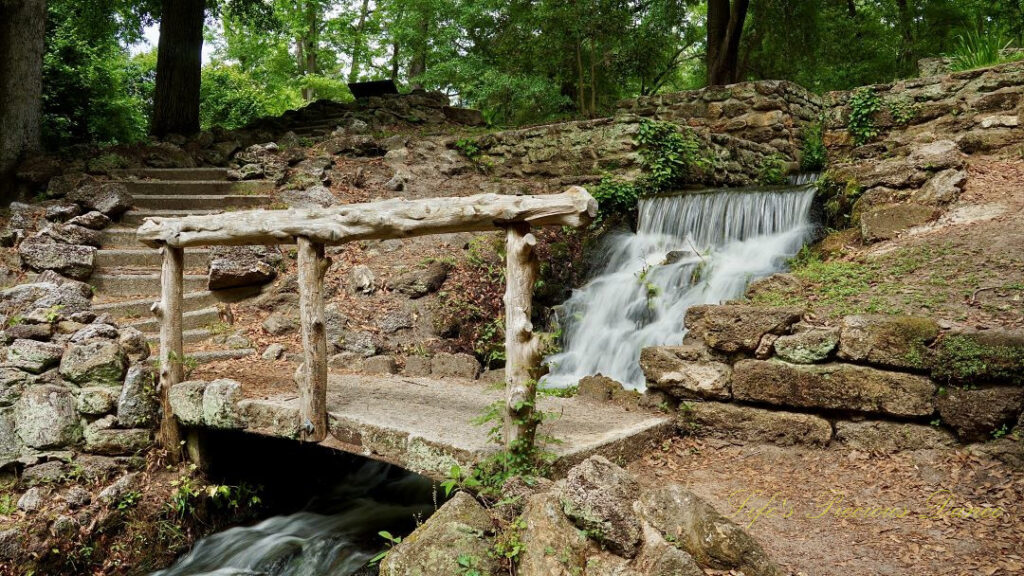 A small stone bridge with wooden guardrails crossing in front of the mini-waterfall at Poinsett State Park. Surrounded by the old mill remnants.