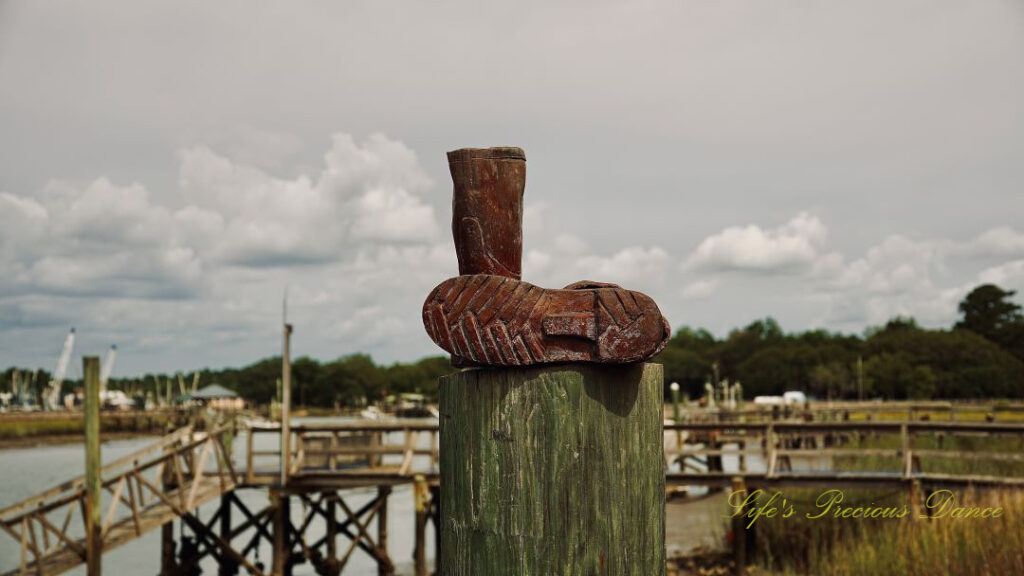 A pair of boots resting, in an L shape, on top of pier post at Jeremy Creek Landing. Passing clouds and a pier in the background.