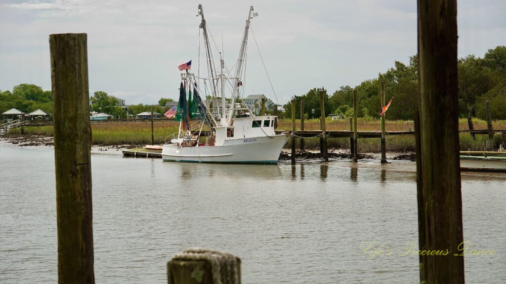 Shrimp boat tied to a dock at Jeremy Creek Landing, framed through two pier posts.