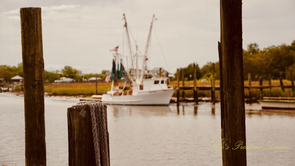 Shrimp boat tied to a dock at Jeremy Creek Landing, framed through two pier posts. A rope is draped over one of the posts