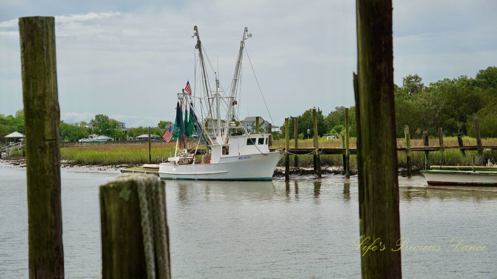 Shrimp boat tied to a dock at Jeremy Creek Landing, framed through two pier posts. A rope is draped over one of the posts