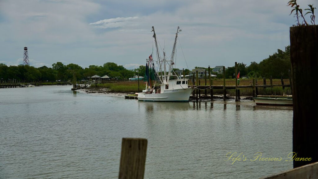 Shrimp boat tied to a dock at Jeremy Creek Landing. Clouds overhead and a water tower in the the distance.