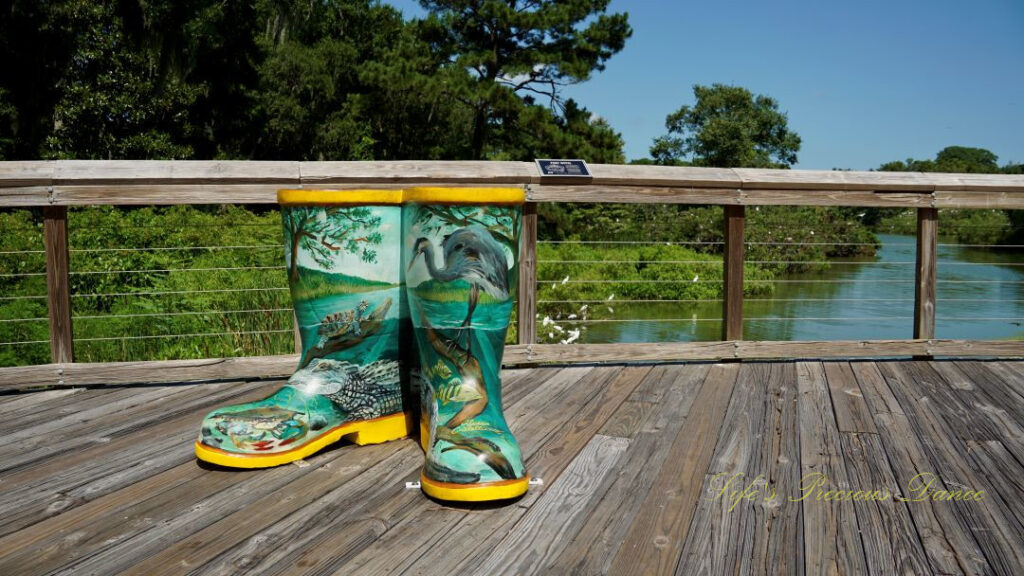 Boot sculptures, painted with the wildlife of the wetlands, on a deck overlooking the water.