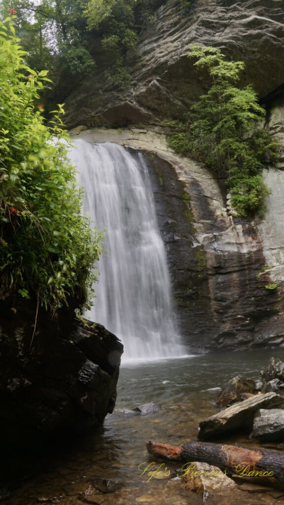 Looking Glass Falls, partially blocked by a boulder, spilling into the awaiting creek below.