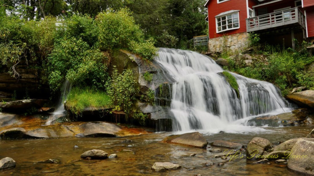 Mill Shoal Falls spilling over rocks into a pool of water. Red cabin above and rocks scattered in the foreground.