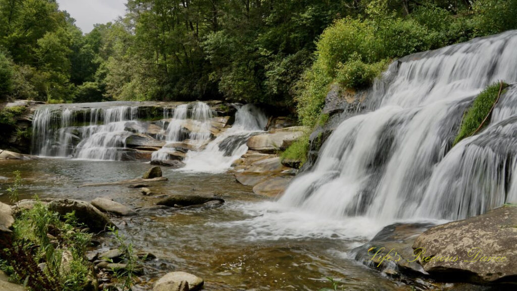 Landscape view of Mill Shoals and French Broad Falls spilling into the river. Rocks scattered throughout the water.