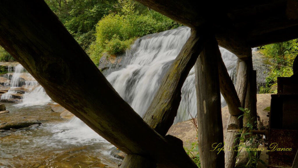 Mill Shoal Falls framed through the wooden posts of a deck. Part of French Broad Falls can be seen to the left.