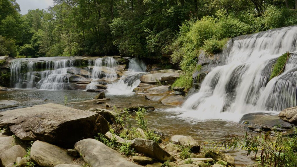 Landscape view of Mill Shoals and French Broad Falls spilling into the river. Rocks scattered throughout the water.