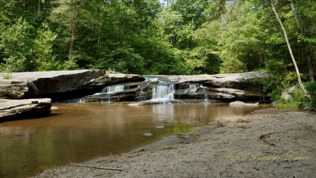 Horseshoe Falls spilling over rocks into the Enoree River. A sandy beach in the foreground.