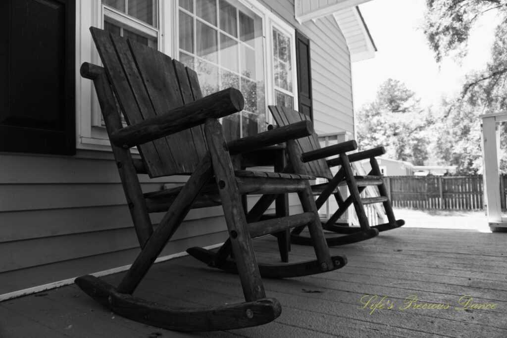 Black and white of wooden rocking chairs on a porch.