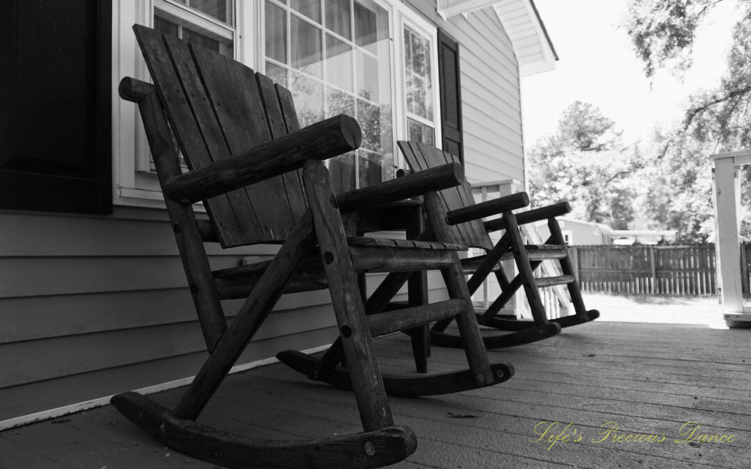 Black and white of wooden rocking chairs on a porch.