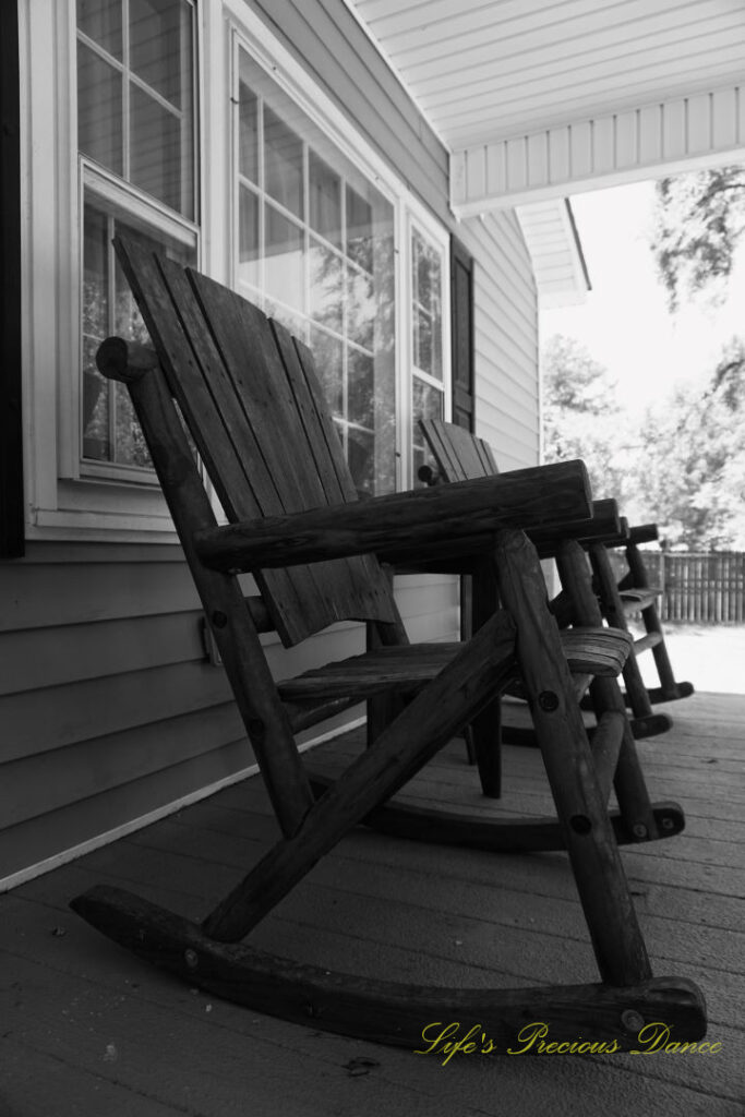 Black and white side view of rocking chairs on a porch.