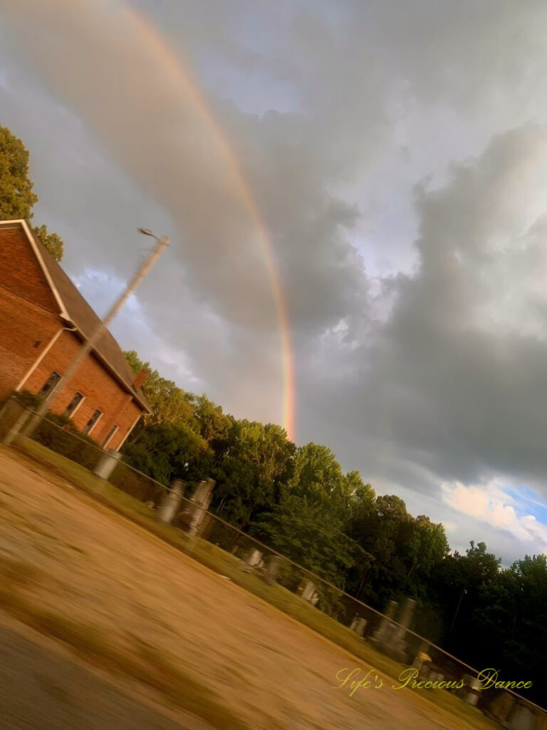 Rainbow stretching over a church and cemetery. Clouds in the background.