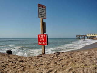 Warning sign to Keep Off Rocks at Edisto Beach State Park. The ocean and pier in the background.