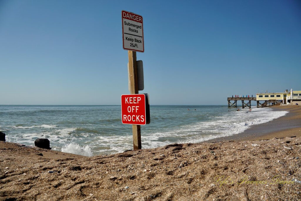 Warning sign to Keep Off Rocks at Edisto Beach State Park. The ocean and pier in the background.