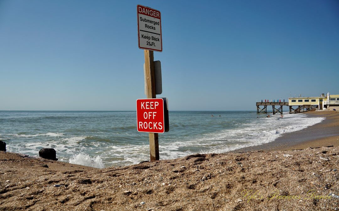 Warning sign to Keep Off Rocks at Edisto Beach State Park. The ocean and pier in the background.