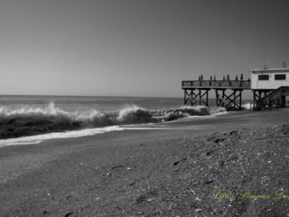 Black and white of waves crashing into the shore at Edisto Beach. The pier stands in the background.