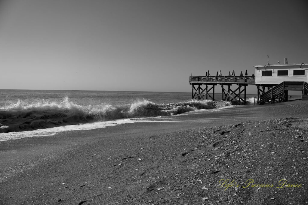 Black and white of waves crashing into the shore at Edisto Beach. The pier stands in the background.