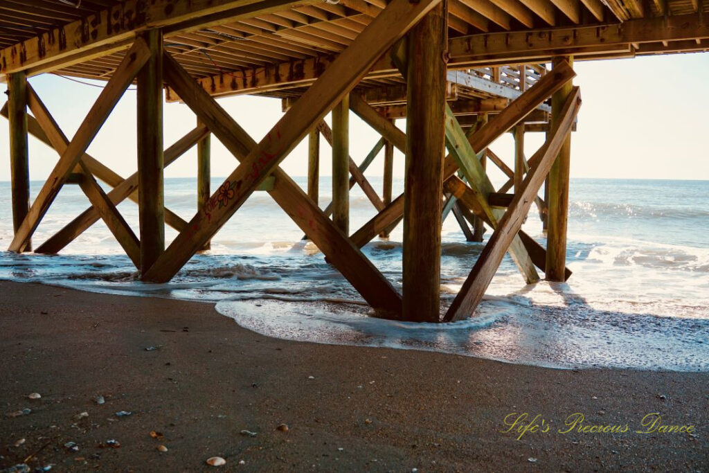 Underside of the pier at Edisto Beach. Seashells in the sand and waves rolling in.