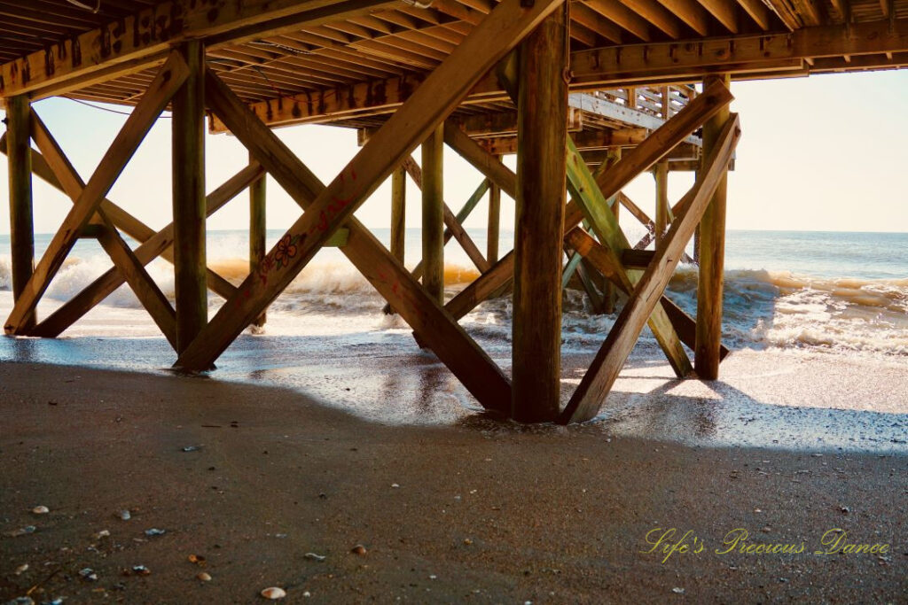 Underside of the pier at Edisto Beach. Seashells in the sand and waves crashing into the shore.