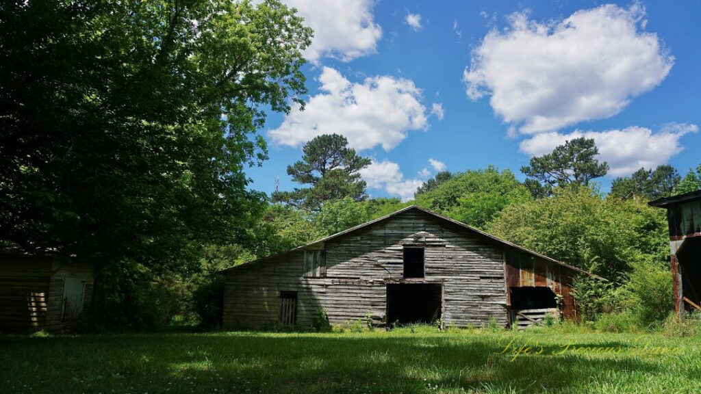 Ground level view of an old barn, Fluffy passing clouds overhead and trees in the background