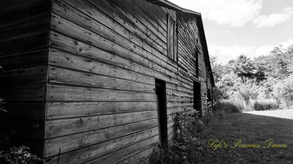 Black and white view of the frontside of a barn. Passing clouds overhead.