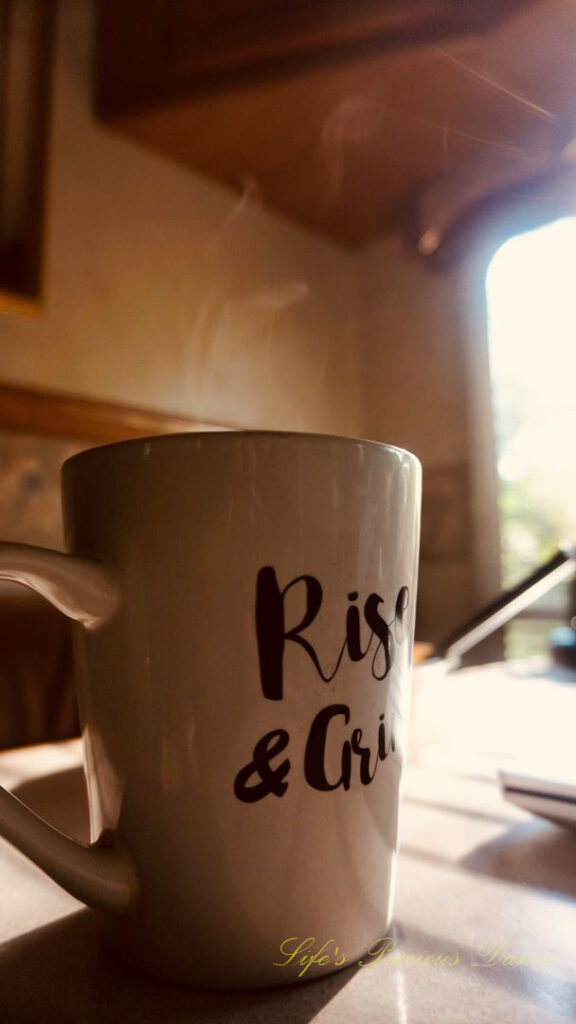 A coffee mug on a table with steam rising from the top. The sun&#039;s rays streaking through a window.