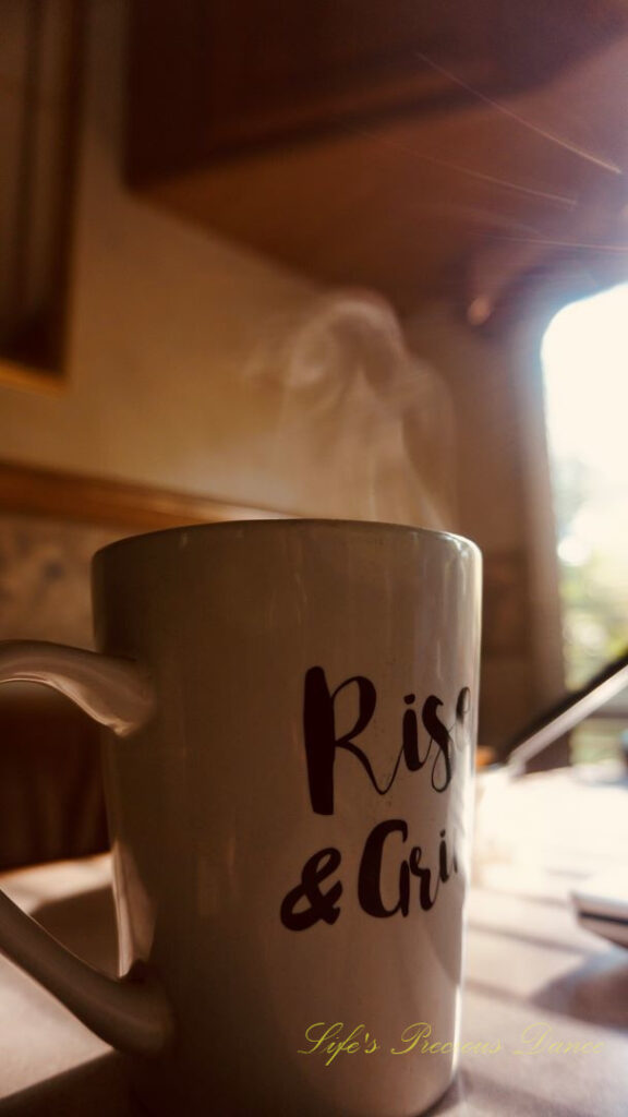 A coffee mug on a table with steam rising from the top. The sun&#039;s rays streaking through a window.