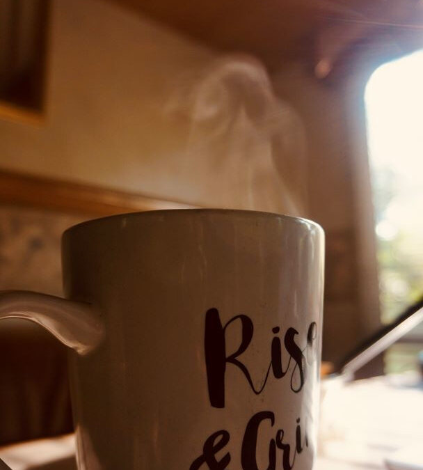 A coffee mug on a table with steam rising from the top. The sun's rays streaking through a window.