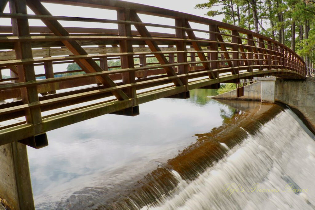 A walking bridge leading over the spillway at Lake Juniper. Clouds reflecting on the water&#039;s surface.