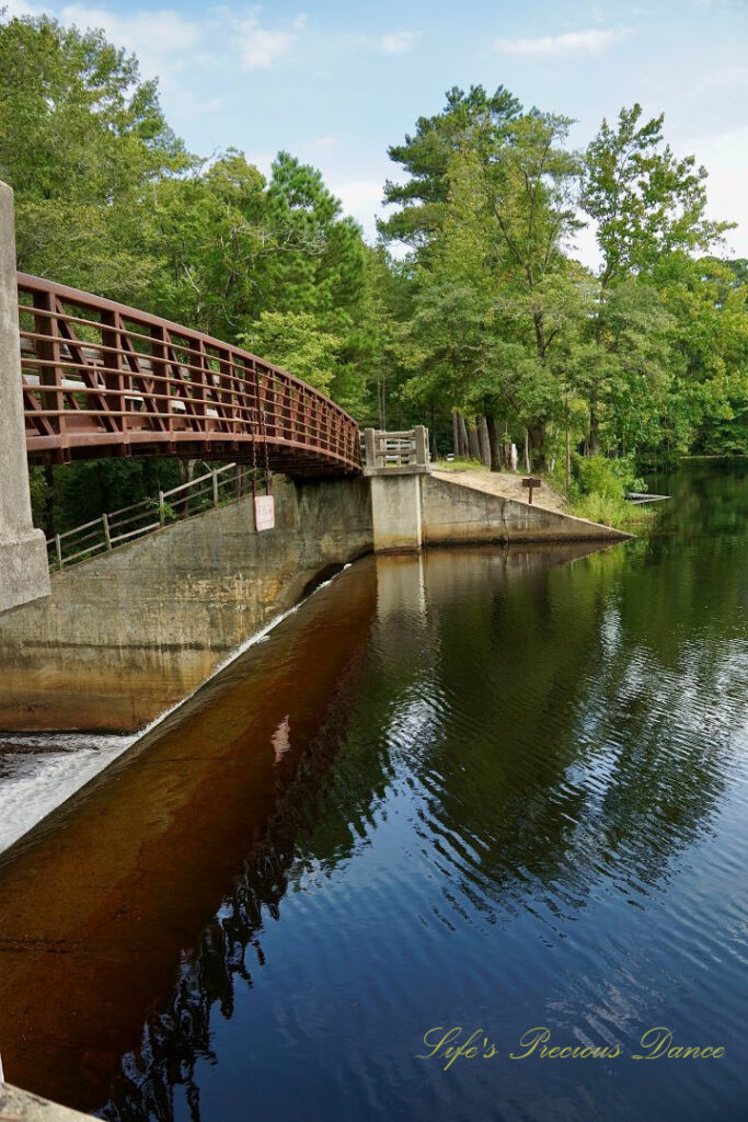 Frontside of a walking bridge leading over the spillway at Lake Juniper. Trees reflecting on the water&#039;s surface.