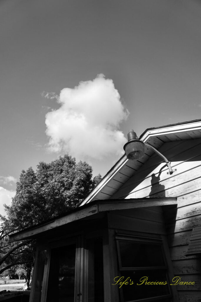 Black and white of the top of a small pottery house. A lone fluffy cloud overhead.